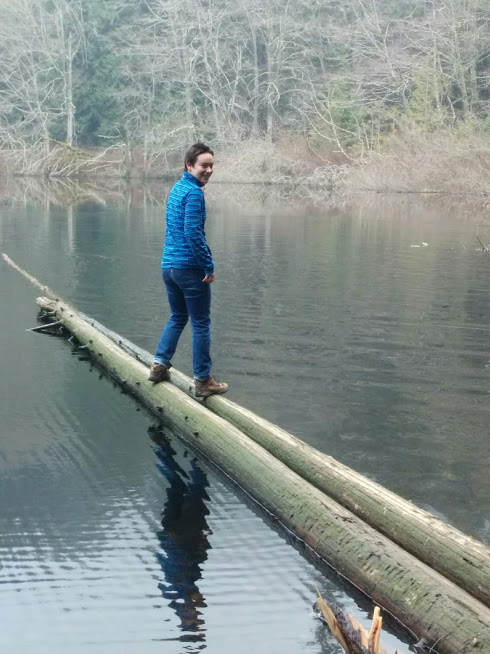 Out on two limbs. Logs. Woman balanced on two logs sticking out into a lake. 